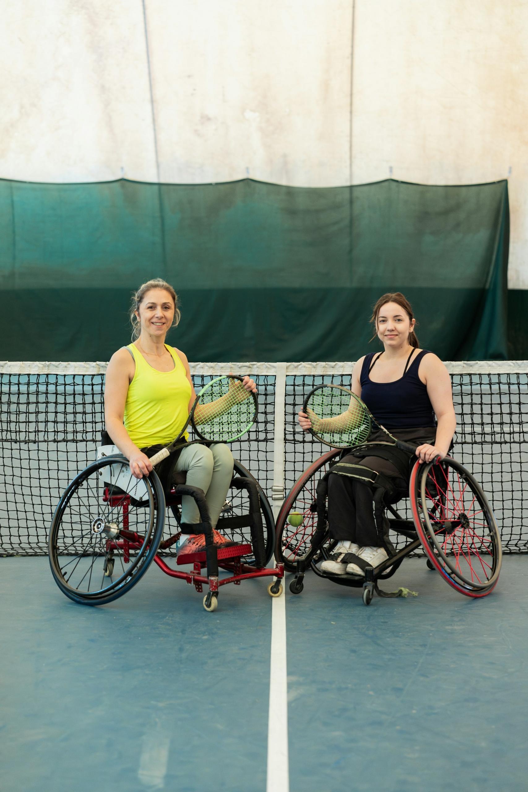 two women in wheelchairs holding tennis rackets on a tennis court